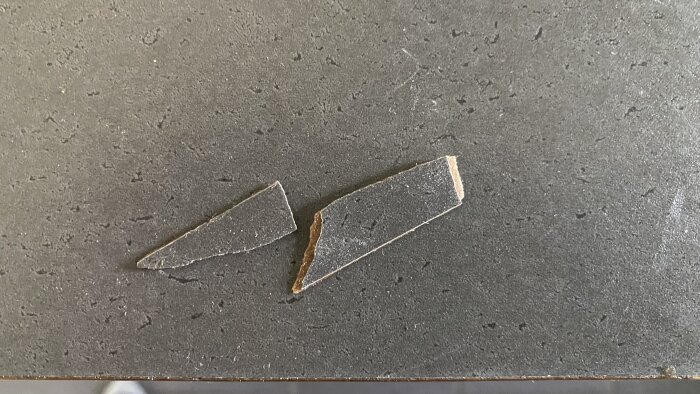 Två avbrutna bitar av ett gråsvart laminatmaterial ligger på en mörk yta.