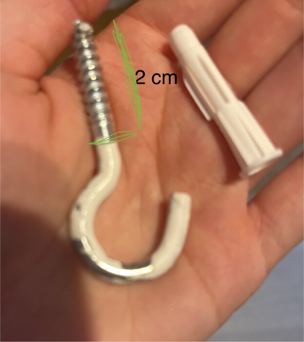 Hand håller en 2 cm krokformad skruv och en vit plastplugg; diskussion om bärkraft för en lampa i betong.