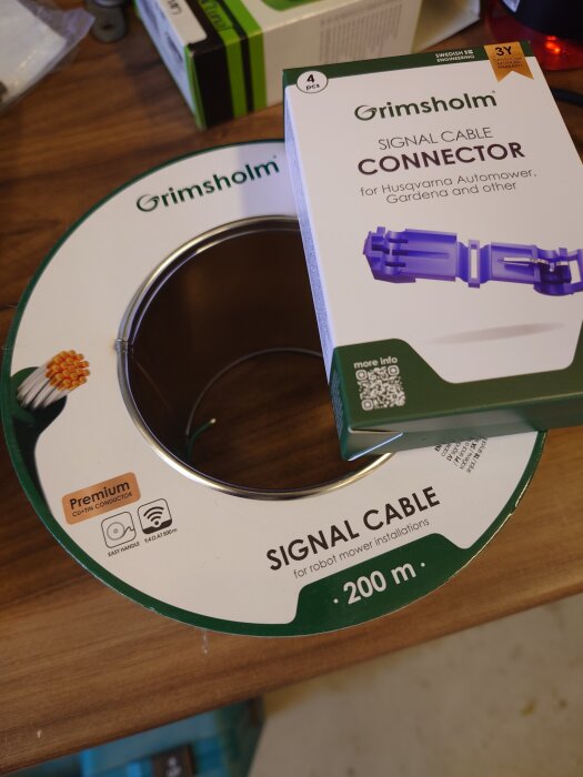 Signal- och kabelanslutningstillbehör för robotgräsklippare från Grimsholm visas på ett träbord.
