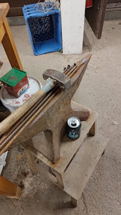 Används smidesstäd och hammare på träpall för kallsmide, bredvid en burk dryck.