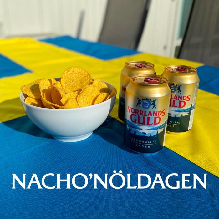 En skål med nachochips och tre burkar alkoholfri Norrlands Guld på svensk flagga, text "Nacho'Nöldagen".