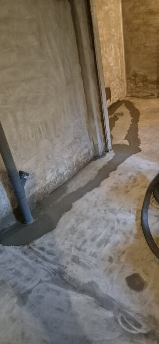 Betonggolv med nyslipade och spacklade skarvar syns, omgiven av väggar och rör samt verktyg för renovering och byggarbete.