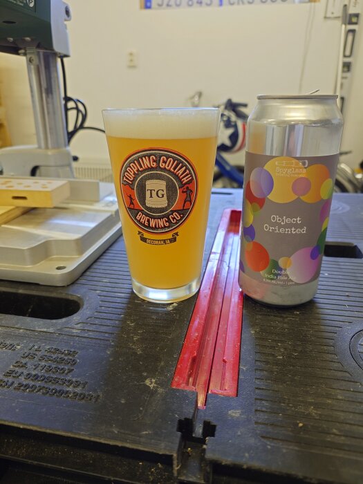 Ett glas öl från Toppling Goliath och en burk Spyglass Object Oriented Double IPA står på en arbetsbänk i ett verkstadsutrymme.