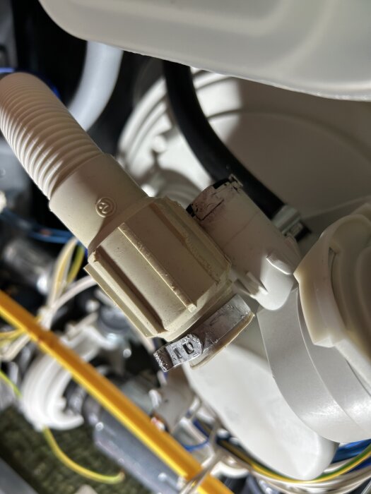 Avloppsslang med en ovanlig slangklämma monterad i en maskin, med omgivande kablar och plastkomponenter.