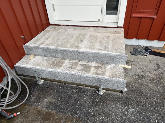 Betongtrappa med två sättsteg på plats framför en röd träfasad och vit dörr.