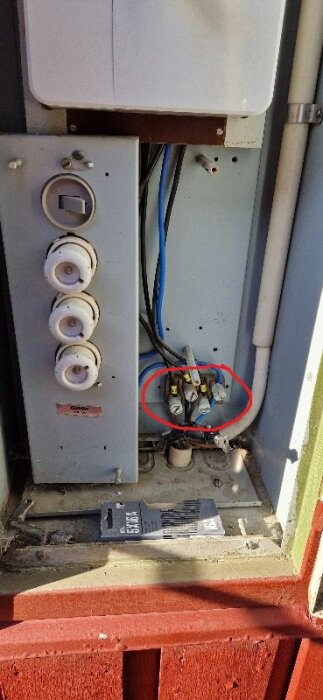 Elcentral med öppet skåp som visar flera vita och blå kablar kopplade till anslutningar. Ett område är markerat med röd cirkel.