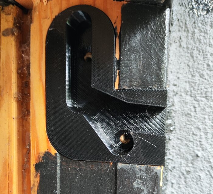 3D-printat fönsterfäste i svart plast monterat på en träram.