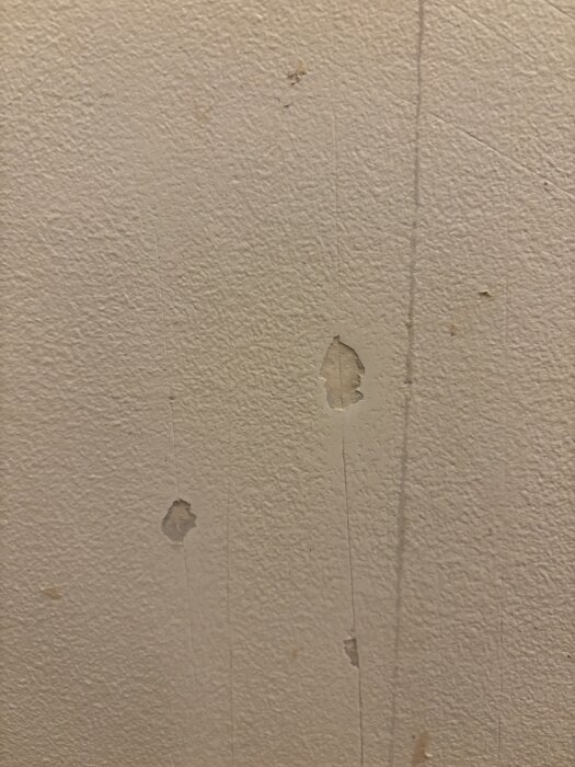 Vägg med bubblig och skadad plastfärg efter tapetborttagning, synliga fläckar och upphöjningar i ytan.