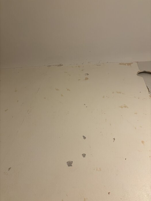 Vägg i hall med uppluckrad plastfärg, synliga bubblor och avskavda partier efter borttagning av tapet.