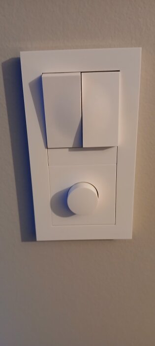 Väggmonterad vit tryckdimmer och strömbrytare på en beige vägg.