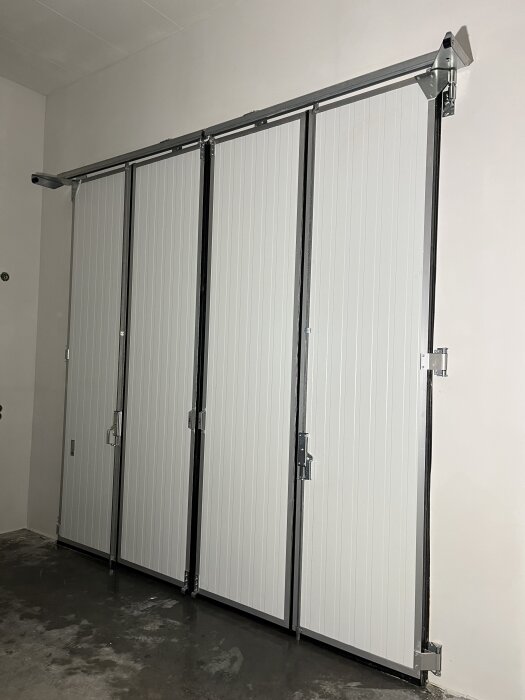 Inåtgående 4-bladig Prido-port monterad i ett rum med vit vägg och betonggolv.