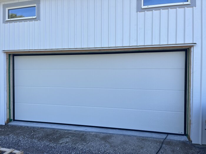 Vit takskjutsport monterad på en byggnad med ljus träpanel och två små fönster ovanför porten.