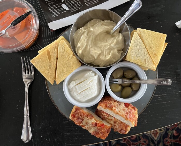 Tapas tallrik med hummus, bröd, mozzarella, oliver och brödbitar med ost och tomat.
