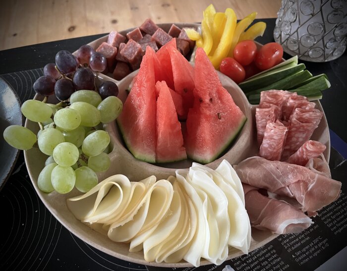 En tallrik med tapas: vattenmelon, vindruvor, gurka, paprika, körsbärstomater, ostskivor, salami, prosciutto och charkuterier.
