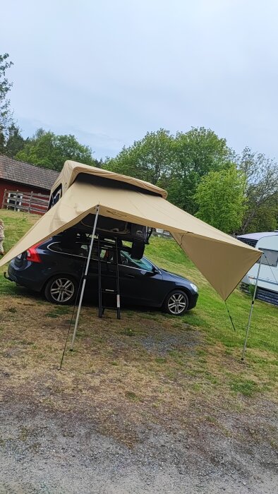 Bil med uppställd tarp som tält och stege bredvid i en trädgård.