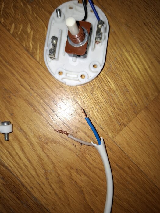 Gammal kontakt med kabel, där trådarna är blottlagda, på ett trägolv.