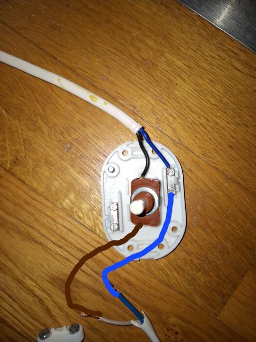 Elektrisk kopplingsplatta med brun och blå ledning på träunderlag, med brun och blå ritade linjer som visar hur kopplingen ska ske.