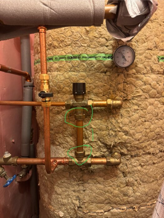 Kopparrör och ventilanslutning vid ackumulatortank med isolering och en termometer som visar temperaturen, omgivna av gröna markeringar.
