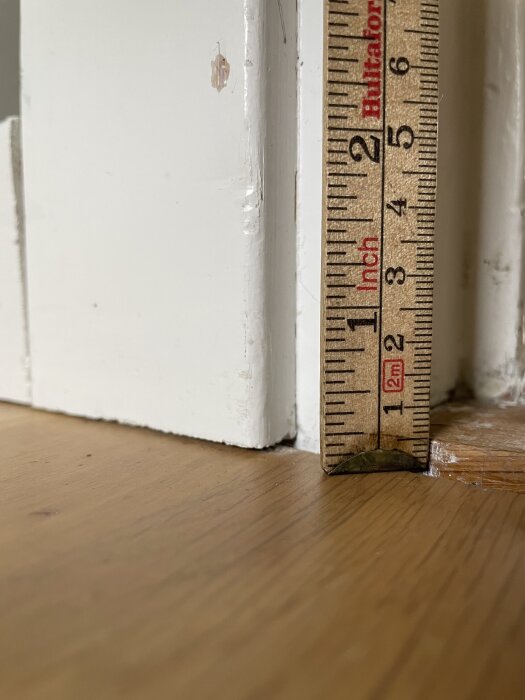 Glipa mellan golv och vit tröskel mäts med måttstock som visar avståndet.