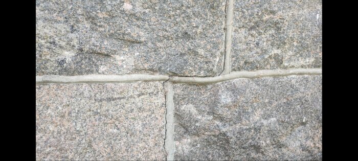 Detalj av en murvägg med synliga sprickor i murbruket mellan stenarna.