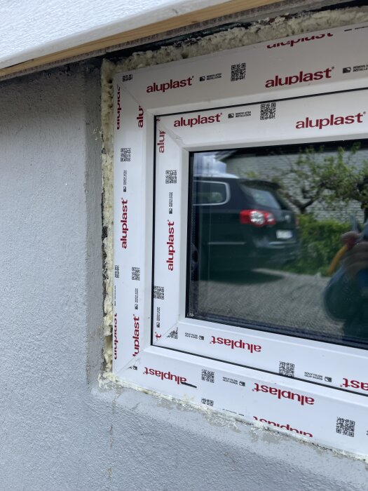 Närbild på ett nyinstallerat PVC-fönster med aluminiumkärna. Fogmassa syns runt fönstret och en bred glipa är synlig i öppningen.