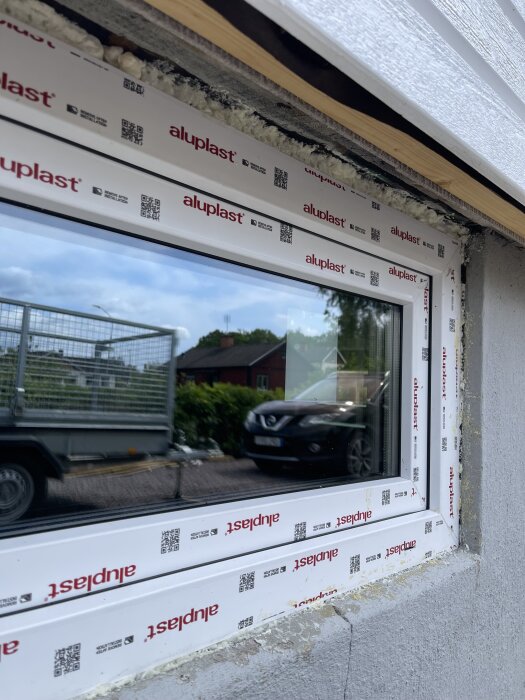 Nytt PVC-fönster med aluminiumkärna installerat i källaren, synligt fogskum och utvändiga anpassningar för bredare karmar.