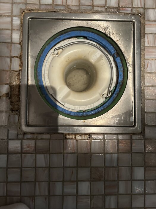 Närbild på golvbrunn med lösa klinkerbitar runtom, visar avsaknad av fog på vänster sida.