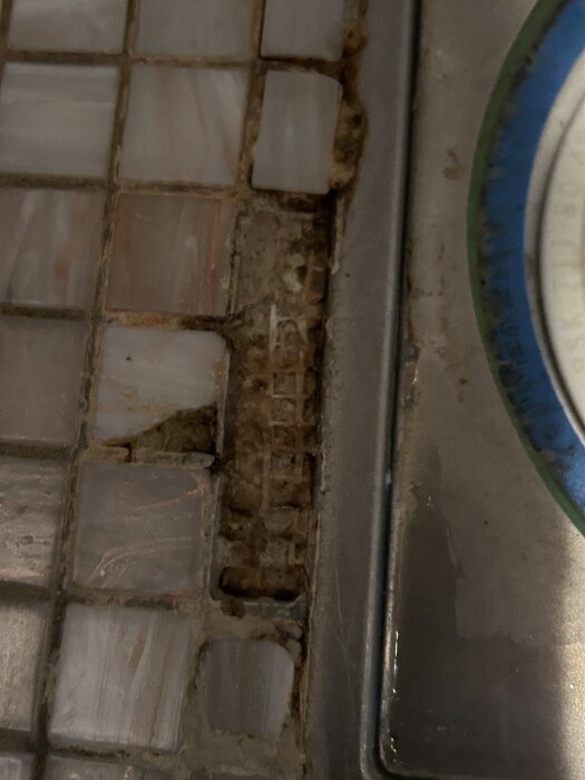 Badrumsgolv med klinkerplattor som lossnat, särskilt runt avloppet, med fogning och skador synliga.