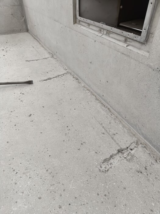 Sprucken betong mellan bänk och vägg upptagen med bilmaskin, före spackling; synligt fönster till höger.
