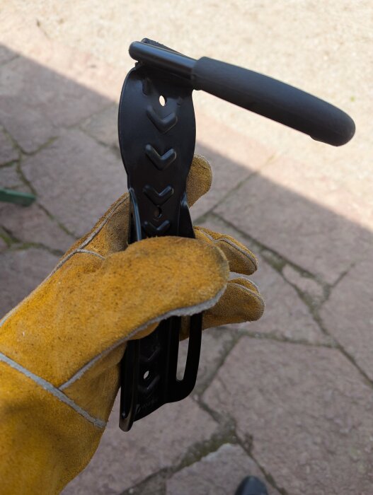 Hand i arbetshandske håller en svart cykelhållare med fästkrok, del av cykelprojekt.