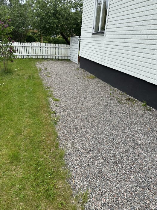 Grusgång bredvid ett vitt tegelhus, omgiven av gräsmatta och staket.