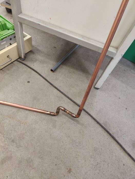 Kopparrör med improviserad böjning i garage, draget för att nå en blandare, syns på betonggolv.