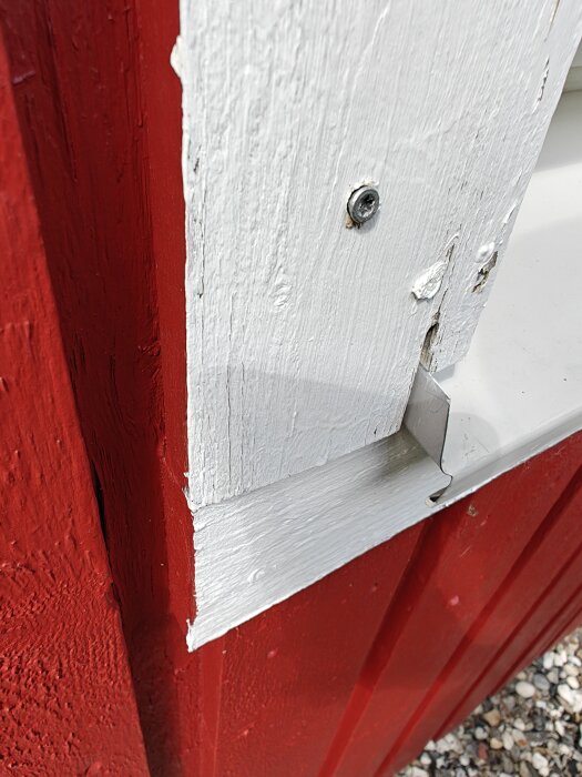 Röd vägg med vitt foder och en synlig trallskruv som inte dragit i det vita träet.