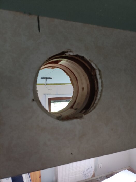 Ett runt hål i en vägg ovanför en innerdörr, med träkanter synliga, i ett rum som verkar vara under renovering.