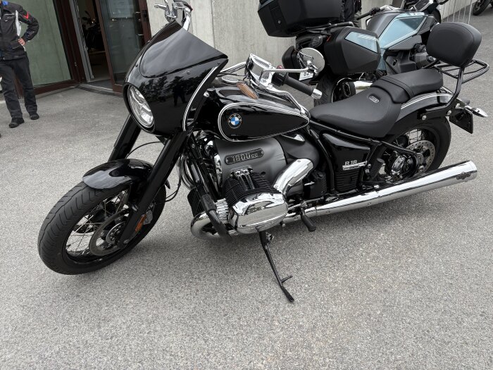 Svart motorcykel med kromdetaljer parkerad utomhus, tagen snett framifrån, redo för provkörning.
