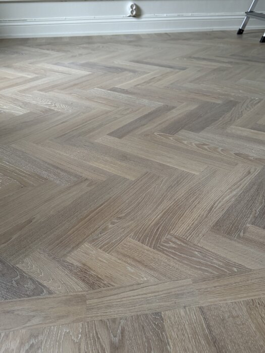 Parkettgolv i fiskbensmönster, synliga märken och vitflammighet.