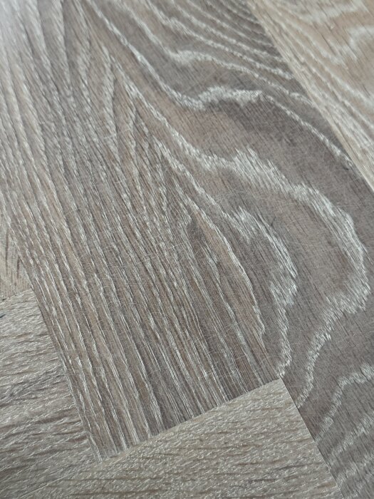 Närbild av ett parkettgolv med synliga slipmärken och vitflammiga partier.