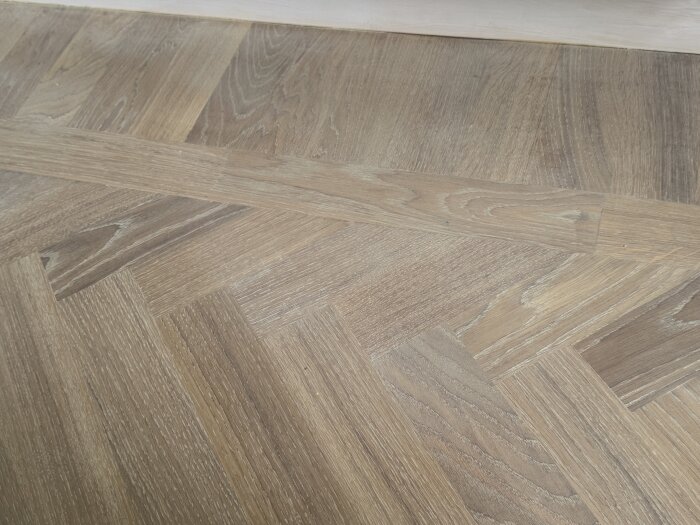 Närbild på trägolv med fiskbensmönster, visar vita flammiga märken och några mörka sliprosor efter flera slipningar.