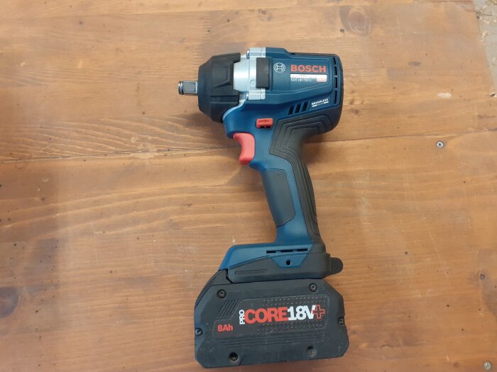 En Bosch GDS 18V-750 C mutterdragare ligger på ett träbord, utrustad med ett 18V batteri.