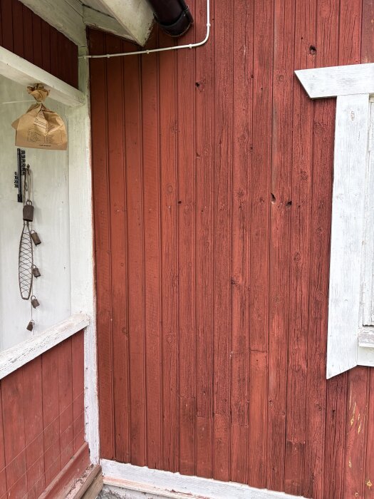 Röd träfasad med vitmålade detaljer och sprickor synliga, del av sommarhus från 1900-talet.