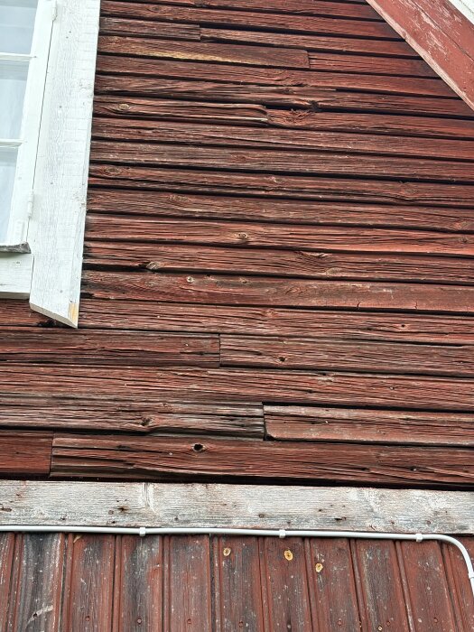 Sliten röd träfasad från ett gammalt sommarhus, med sprickor och ojämna plankor.