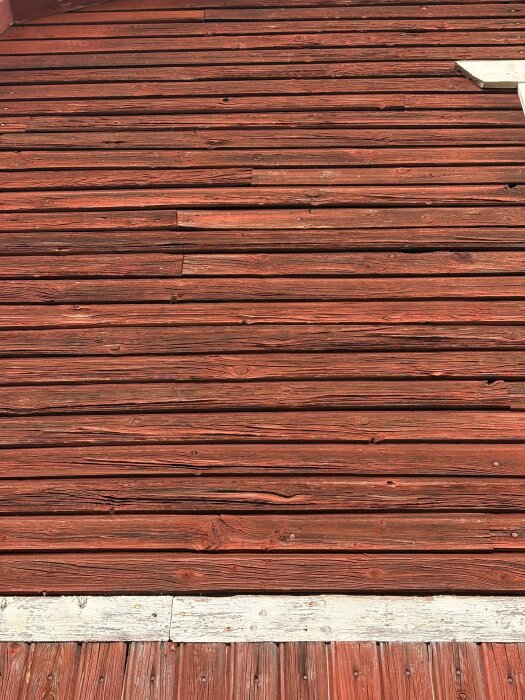 Röd träfasad med liggande paneler, vissa med sprickor, från ett sommarhus byggt runt år 1900.