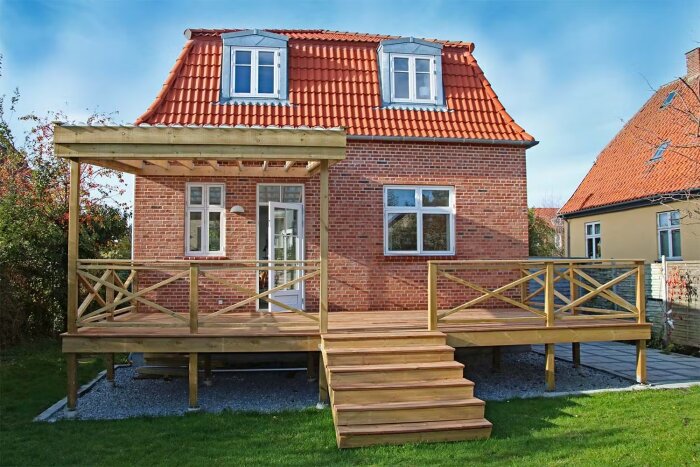 Rött tegelhus med rött tak och en nybyggd träaltan med räcke och trappa.