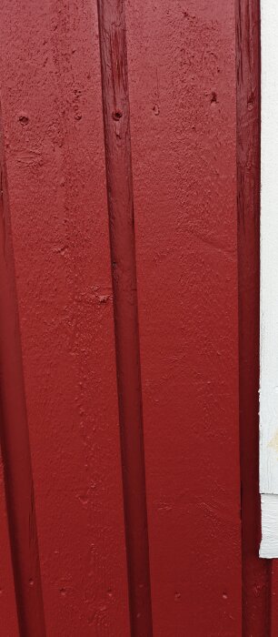 Röd träfasad med synliga spår efter spikar och en vit kant på höger sida. Visar diskuterade foder och spikreglar.