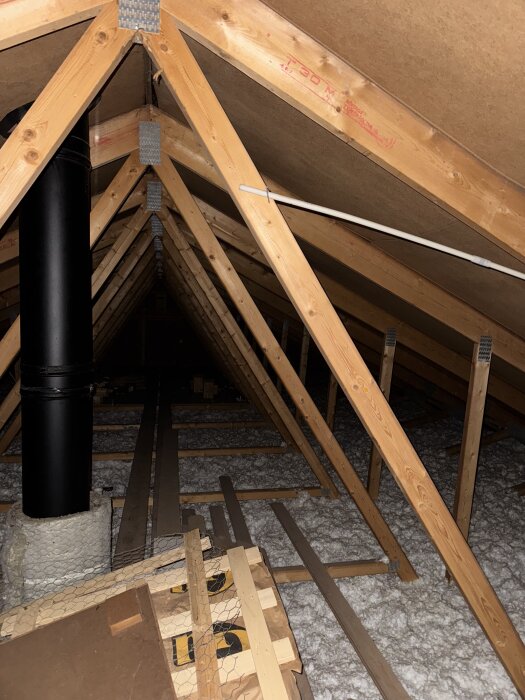 Vind med träbalkar, isolering och svart ventilationsrör.