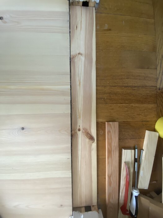 Träplanka som täcker del av golvöppning, omringad av verktyg och träbitar. Problem med stabilitet och täckning av hela bredden syns tydligt.