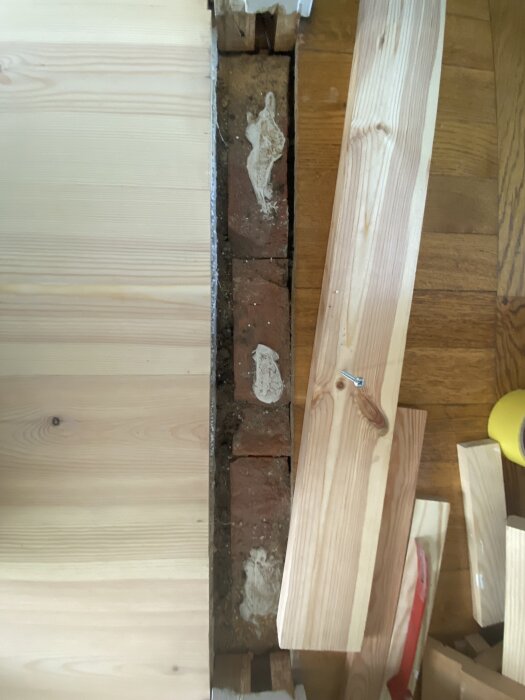 Trägolv med synligt öppet hål över tegel och bräda som ska användas för stabilisering.