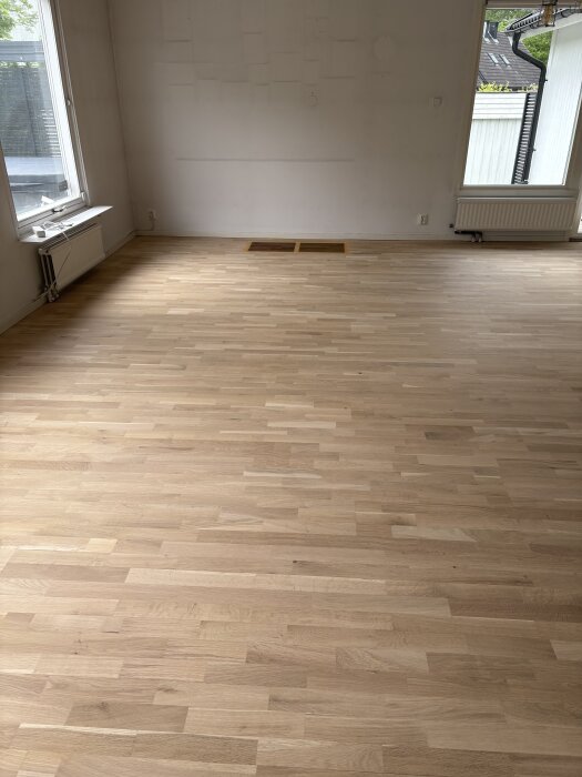 Ljust ekparkettgolv i ett rum med vita väggar och stora fönster.