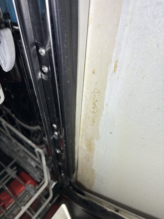 Missfärgning på en vit köksvägg nära en diskmaskin, eventuellt tecken på fuktskada. Diskmaskinens dörr syns delvis på vänster sida.