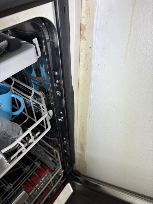 Öppen diskmaskin bredvid en vägg med tydliga missfärgningar och tecken på fuktskada.